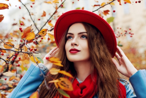 woman in red hat standing amongst autumn foliage