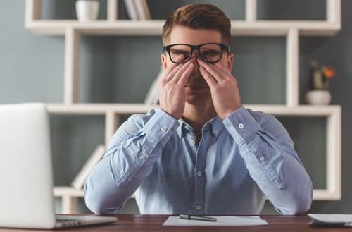 Man rubbing his eyes under glasses