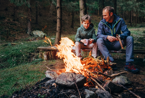 father and son sitting by fire while camping